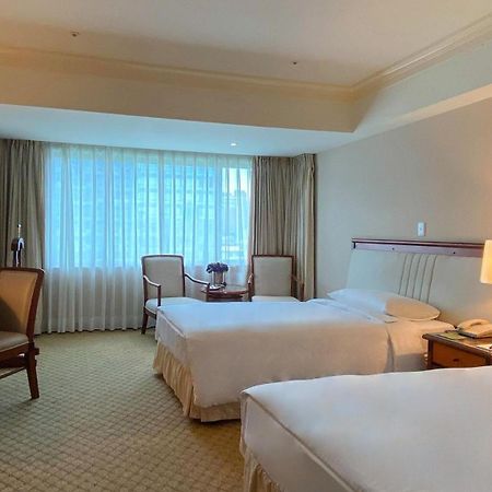 เอเวอร์กรีน เลาเรล โฮเต็ล ไทชุง Hotel ไถจง ภายนอก รูปภาพ The photo shows a hotel room featuring two single beds positioned near each other. There's a light-colored carpet on the floor and a large window with sheer curtains that allows natural light to fill the space. In the room, there are two chairs place