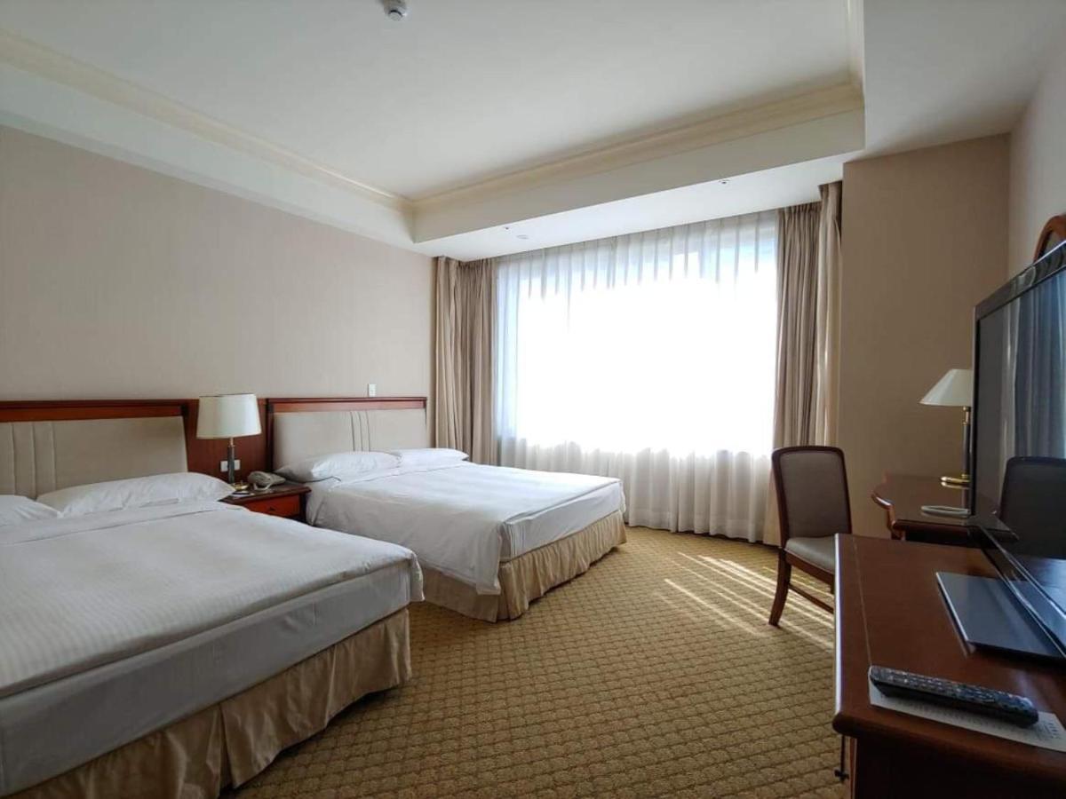 เอเวอร์กรีน เลาเรล โฮเต็ล ไทชุง Hotel ไถจง ภายนอก รูปภาพ The image shows a hotel room featuring two single beds with white bedding. There is a large window with sheer curtains letting in natural light, and the walls are painted in neutral tones. A wooden desk with a chair is positioned near the window, and