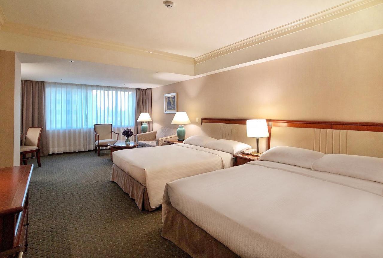 เอเวอร์กรีน เลาเรล โฮเต็ล ไทชุง Hotel ไถจง ภายนอก รูปภาพ The photo shows a hotel room featuring two queen-sized beds with white linens. The room is well-lit and has a warm, neutral color palette. There are bedside lamps on each side of the beds and a small table. To the side, there's a comfortable armchair