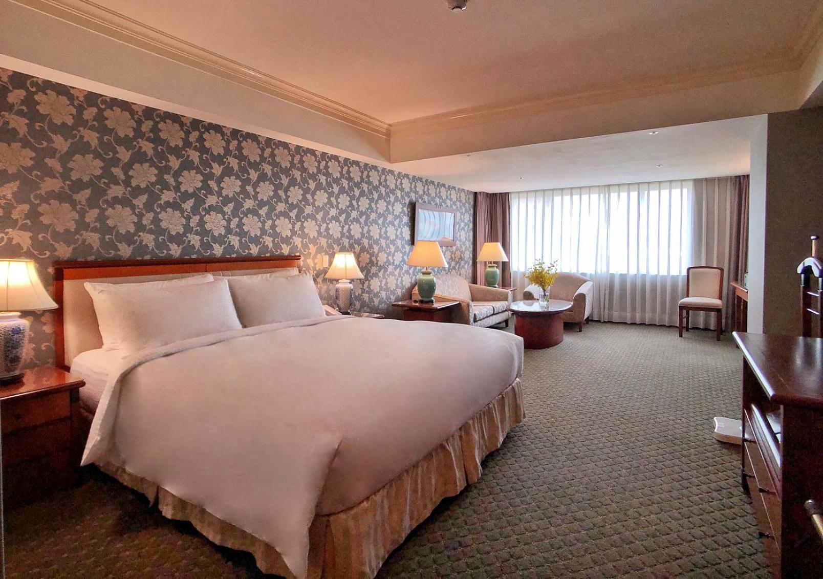 เอเวอร์กรีน เลาเรล โฮเต็ล ไทชุง Hotel ไถจง ภายนอก รูปภาพ The photo shows a hotel room with a spacious and comfortable layout. It features a large bed with white bedding, placed against a decorative wallpapered wall. On either side of the bed, there are lamps providing soft lighting. In addition to the bed,