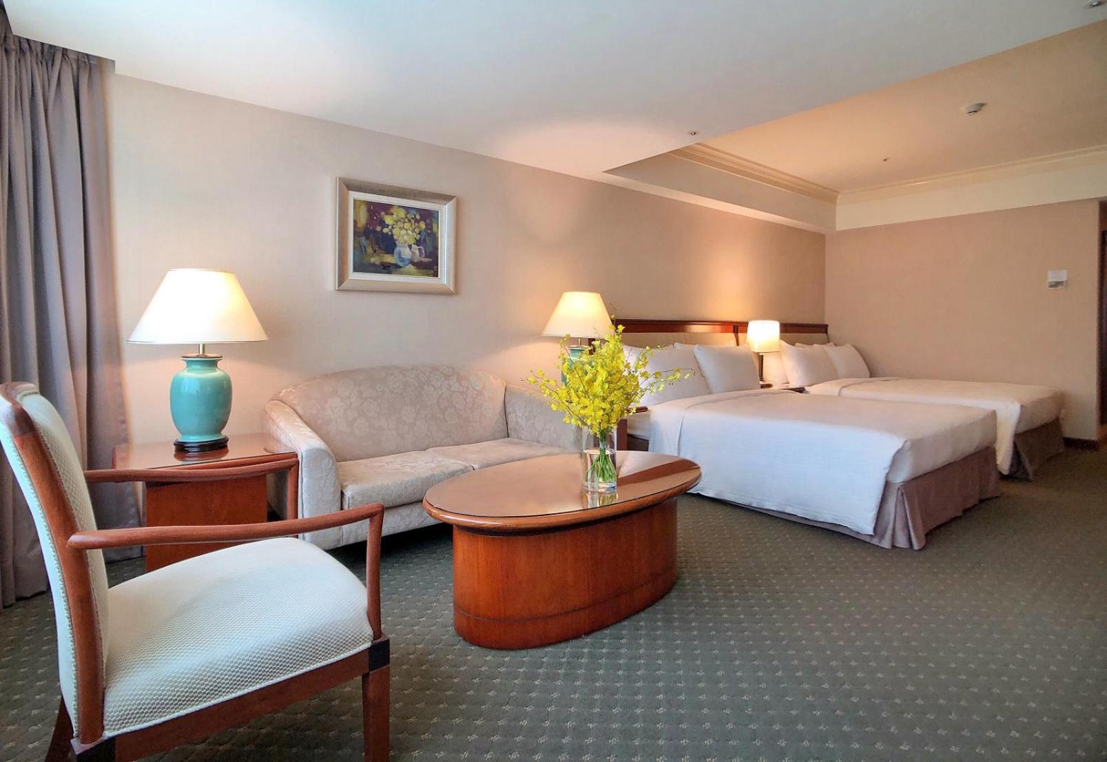 เอเวอร์กรีน เลาเรล โฮเต็ล ไทชุง Hotel ไถจง ภายนอก รูปภาพ The photo shows a hotel room featuring two beds, a small seating area, and a coffee table. The walls are painted in soft, neutral colors, and there is a framed piece of artwork hanging on the wall. A potted plant with yellow flowers is placed on the 