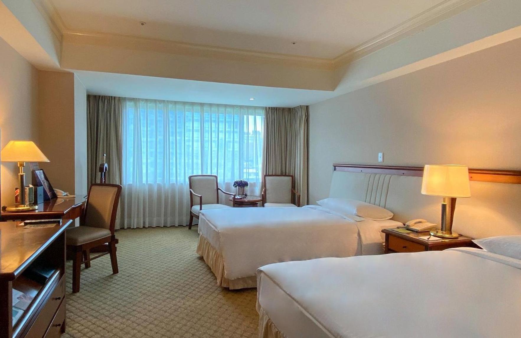 เอเวอร์กรีน เลาเรล โฮเต็ล ไทชุง Hotel ไถจง ภายนอก รูปภาพ The photo shows a hotel room featuring two single beds positioned near each other. There's a light-colored carpet on the floor and a large window with sheer curtains that allows natural light to fill the space. In the room, there are two chairs place
