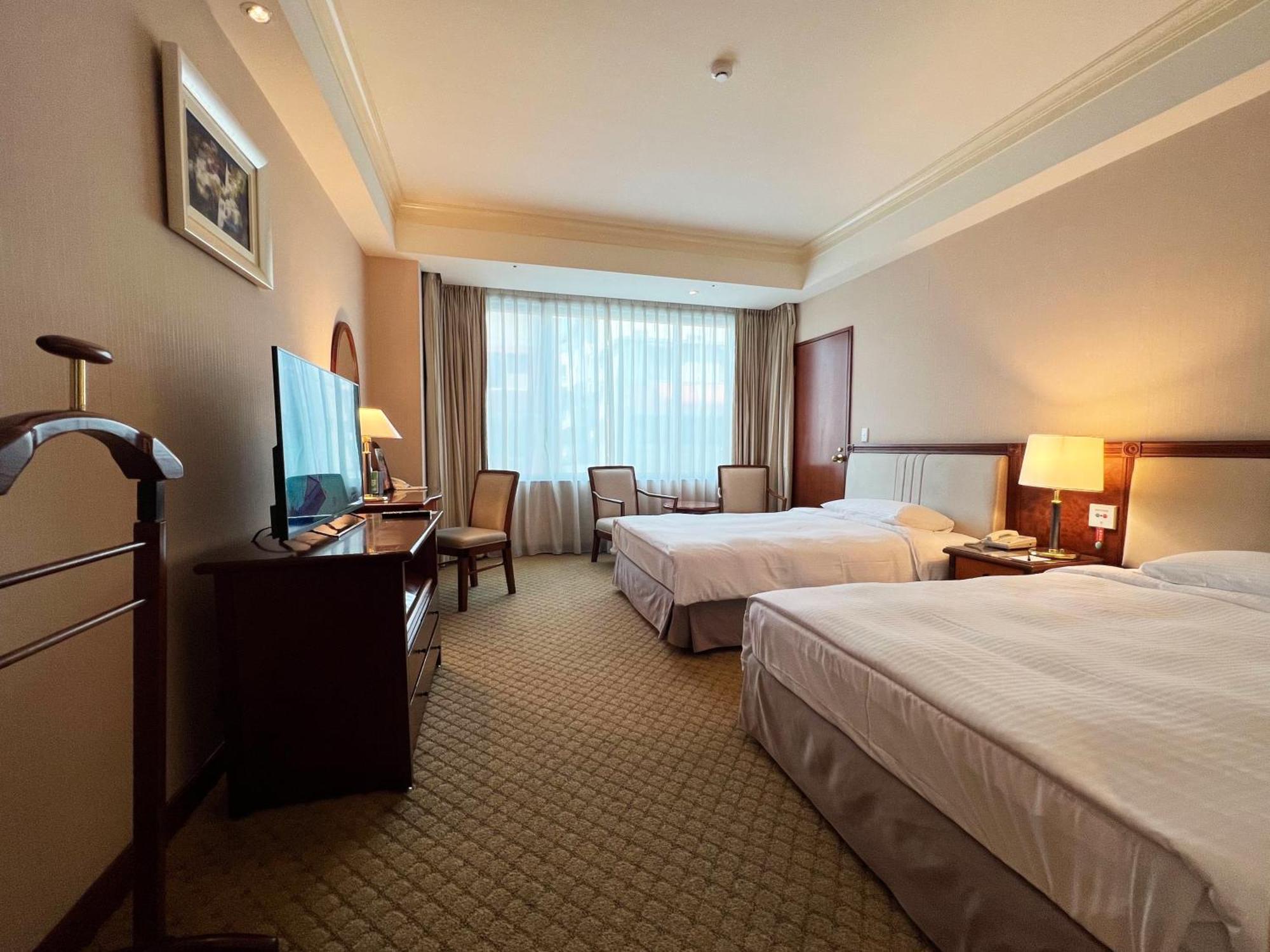เอเวอร์กรีน เลาเรล โฮเต็ล ไทชุง Hotel ไถจง ภายนอก รูปภาพ The photo shows a hotel room featuring two twin beds placed parallel to each other. The room has a warm color palette and includes a large window with sheer curtains allowing natural light to illuminate the space. There is a wooden desk and two chair