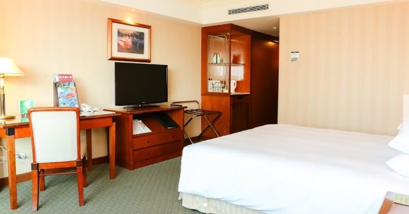 เอเวอร์กรีน เลาเรล โฮเต็ล ไทชุง Hotel ไถจง ภายนอก รูปภาพ The photo shows a hotel room featuring a neatly made bed with a white blanket. On one side, there is a wooden desk with a chair, and a flat-screen television is mounted nearby. An accent cabinet is visible, displaying various items. The walls are pai