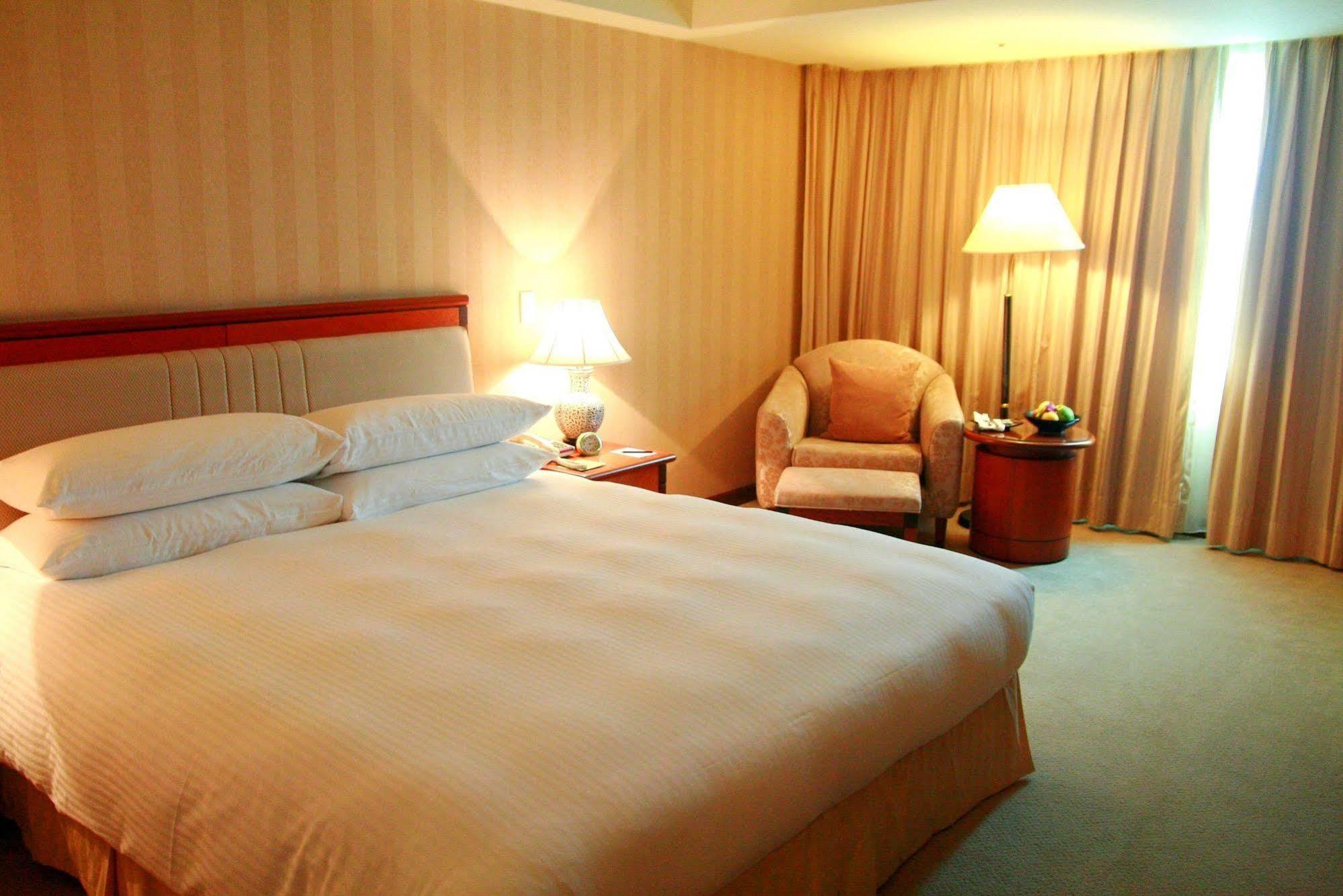เอเวอร์กรีน เลาเรล โฮเต็ล ไทชุง Hotel ไถจง ภายนอก รูปภาพ The photo shows a hotel room containing a large bed with white linens, flanked by two bedside lamps. To one side, there is a cozy armchair and a small side table with a fruit bowl or snacks. The walls are decorated in a soft, neutral color, and there
