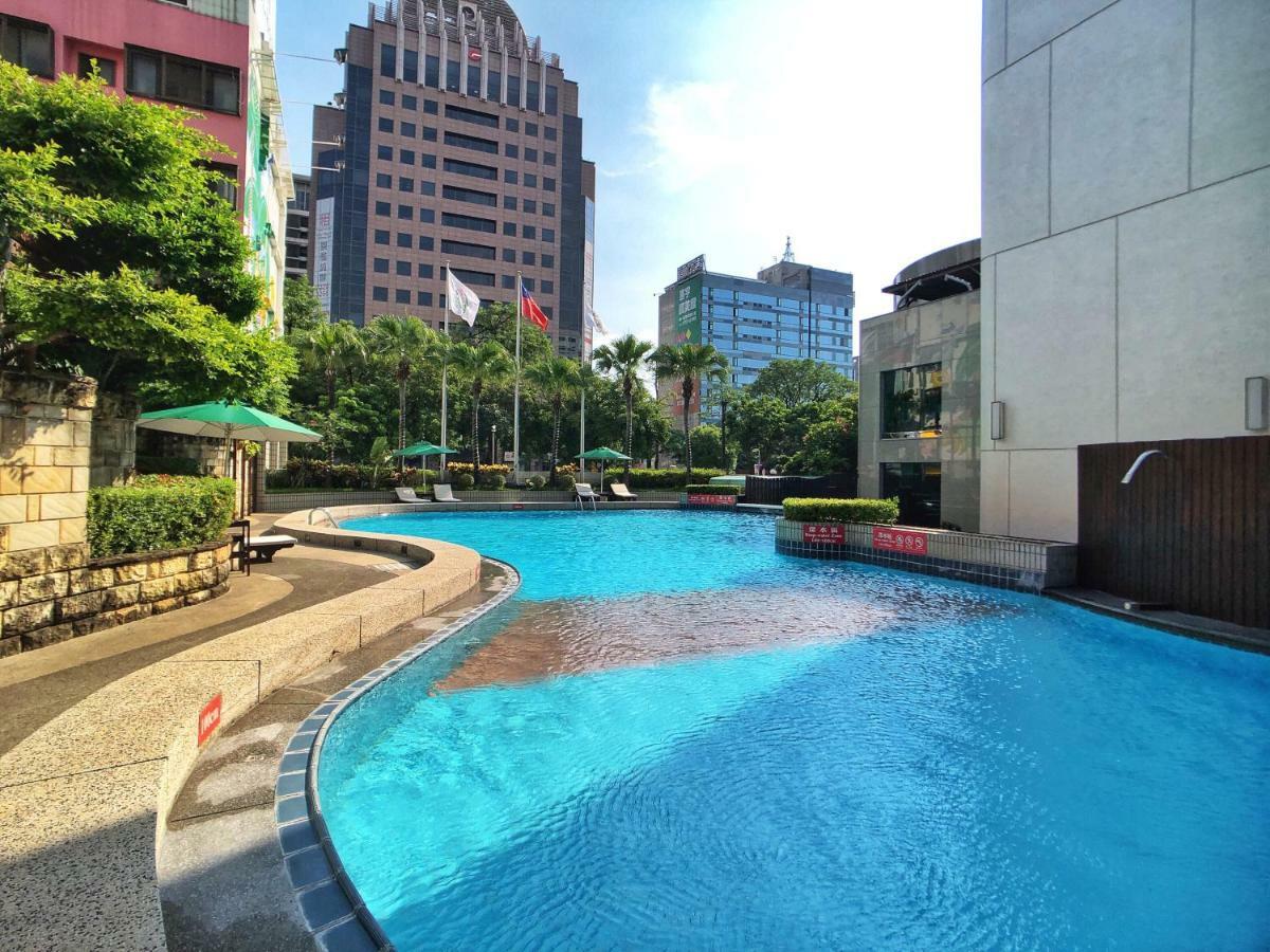 เอเวอร์กรีน เลาเรล โฮเต็ล ไทชุง Hotel ไถจง ภายนอก รูปภาพ The photo shows a swimming pool set in a modern urban environment. The pool has a curved edge and is surrounded by greenery, including trees and umbrellas for shade. In the background, there are several tall buildings, indicating a cityscape, with so