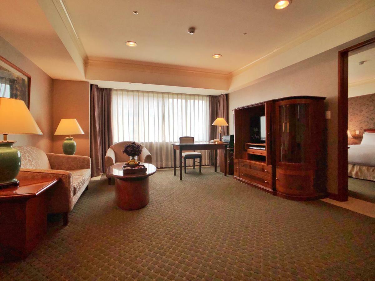 เอเวอร์กรีน เลาเรล โฮเต็ล ไทชุง Hotel ไถจง ภายนอก รูปภาพ The photo shows a cozy hotel suite or living area. There is a sofa and an armchair arranged around a small coffee table. A desk with a chair is positioned near a large window covered with sheer curtains that allow natural light to enter the room. Two