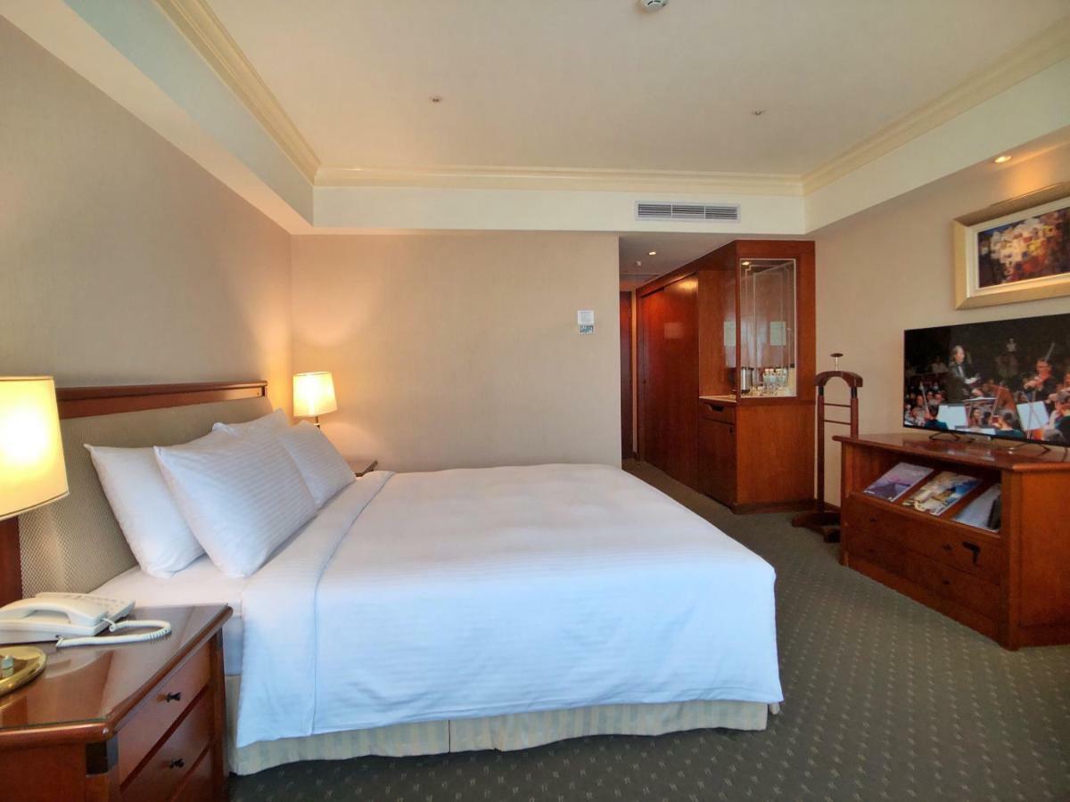 เอเวอร์กรีน เลาเรล โฮเต็ล ไทชุง Hotel ไถจง ภายนอก รูปภาพ The photo shows a hotel room featuring a comfortable bed with white linens and pillows, positioned against a light-colored wall. There is a wooden bedside table with a lamp and an open book next to the bed. On the opposite side, there’s a large flat-