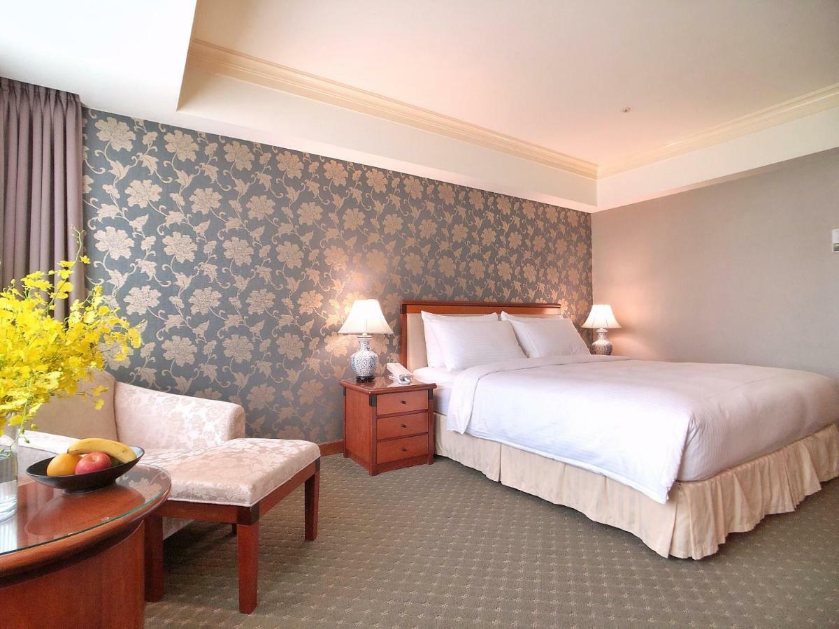 เอเวอร์กรีน เลาเรล โฮเต็ล ไทชุง Hotel ไถจง ภายนอก รูปภาพ The photo shows a well-decorated hotel room. It features a large bed with white bedding, situated against a patterned wall with floral designs. On either side of the bed are bedside tables with lamps. There is a small seating area that includes a cha