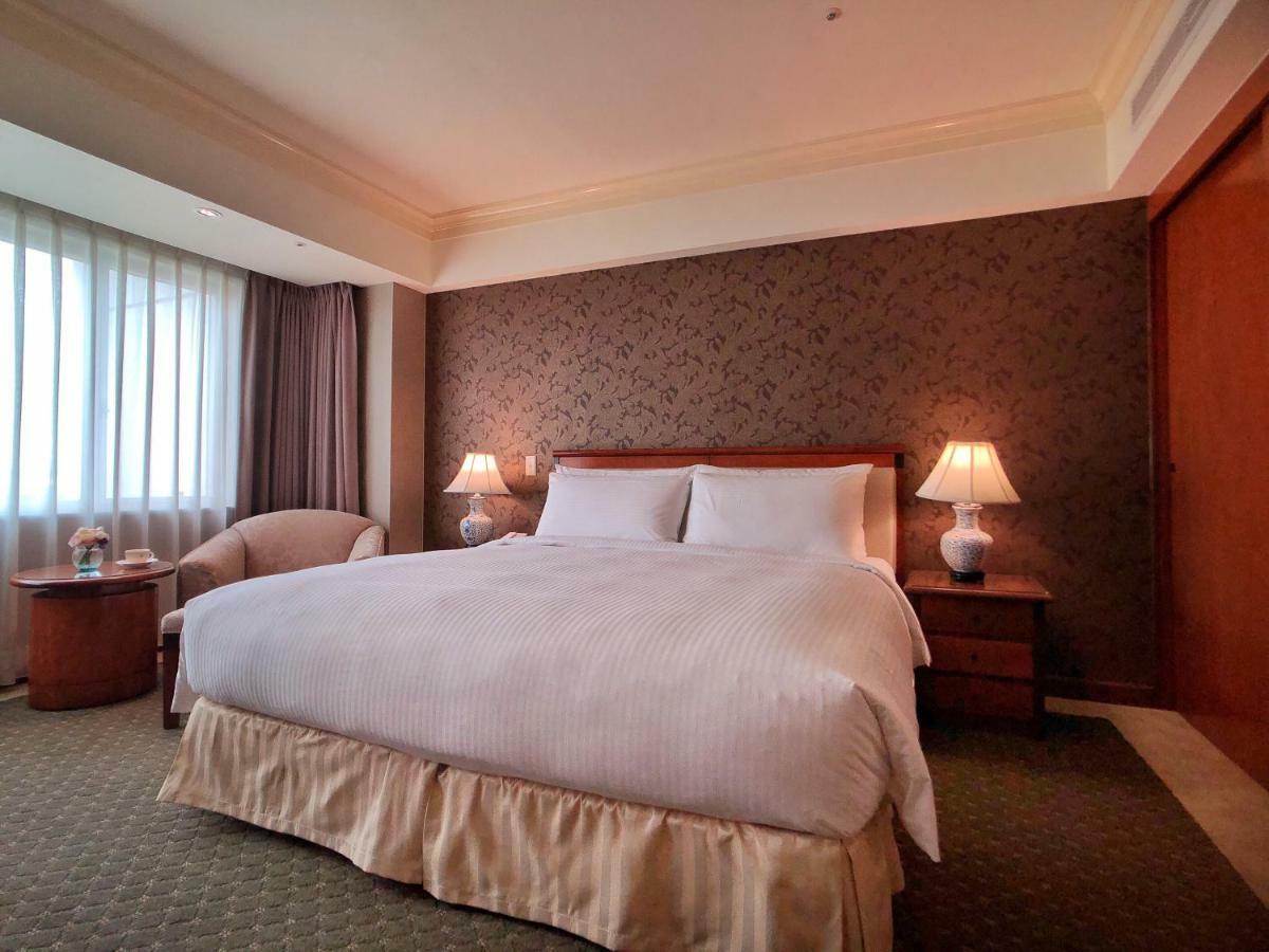 เอเวอร์กรีน เลาเรล โฮเต็ล ไทชุง Hotel ไถจง ภายนอก รูปภาพ The photo shows a neatly arranged hotel room featuring a large bed with white linens and a light-colored bed skirt. On either side of the bed, there are small wooden nightstands with lamps. To the left of the bed, there's a comfortable chair and a ro