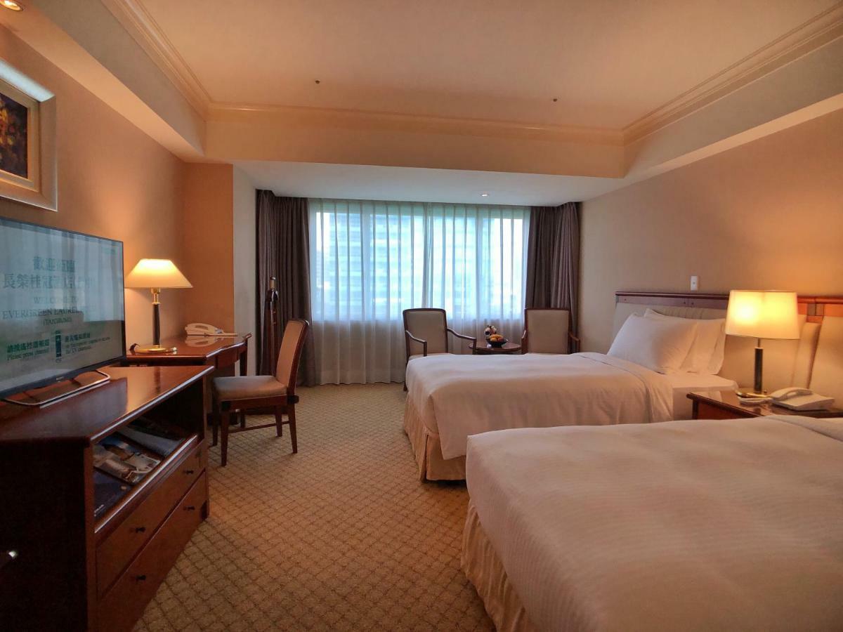 เอเวอร์กรีน เลาเรล โฮเต็ล ไทชุง Hotel ไถจง ภายนอก รูปภาพ The photo shows a hotel room featuring two twin beds with white bedding. There's a television mounted on a wooden dresser, and next to it, a comfortable chair and a small table are positioned. The room has large windows that allow natural light to en