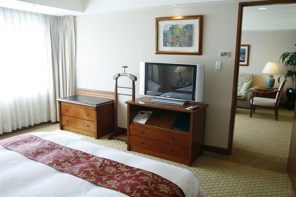 เอเวอร์กรีน เลาเรล โฮเต็ล ไทชุง Hotel ไถจง ภายนอก รูปภาพ The photo depicts a hotel room interior. In the foreground, there is a neatly made bed with a decorative red bedspread. To the left, a large window allows natural light to fill the room, with light-colored curtains drawn to one side. 

Next to the be