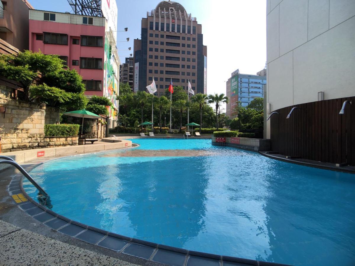เอเวอร์กรีน เลาเรล โฮเต็ล ไทชุง Hotel ไถจง ภายนอก รูปภาพ The photo shows a swimming pool area set in an outdoor environment. The pool has a clear blue water and a gently curving shape. Surrounding the pool are some green trees and plants, along with a few umbrellas providing shade. In the background, there