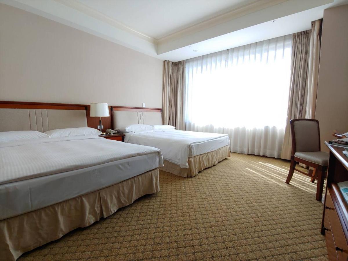 เอเวอร์กรีน เลาเรล โฮเต็ล ไทชุง Hotel ไถจง ภายนอก รูปภาพ The photo shows a neatly arranged hotel room featuring two beds: one double bed and one single bed. The room has beige walls and a warm color palette. Large windows with sheer curtains allow natural light to flood in, creating a bright and airy atmos