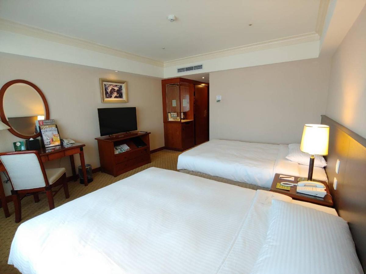 เอเวอร์กรีน เลาเรล โฮเต็ล ไทชุง Hotel ไถจง ภายนอก รูปภาพ The photo shows a hotel room with two beds, neatly made with white linens. There is a desk and chair in one corner, accompanied by a flat-screen TV mounted on the wall. A large mirror and a wooden cabinet are also visible. The room is illuminated by 