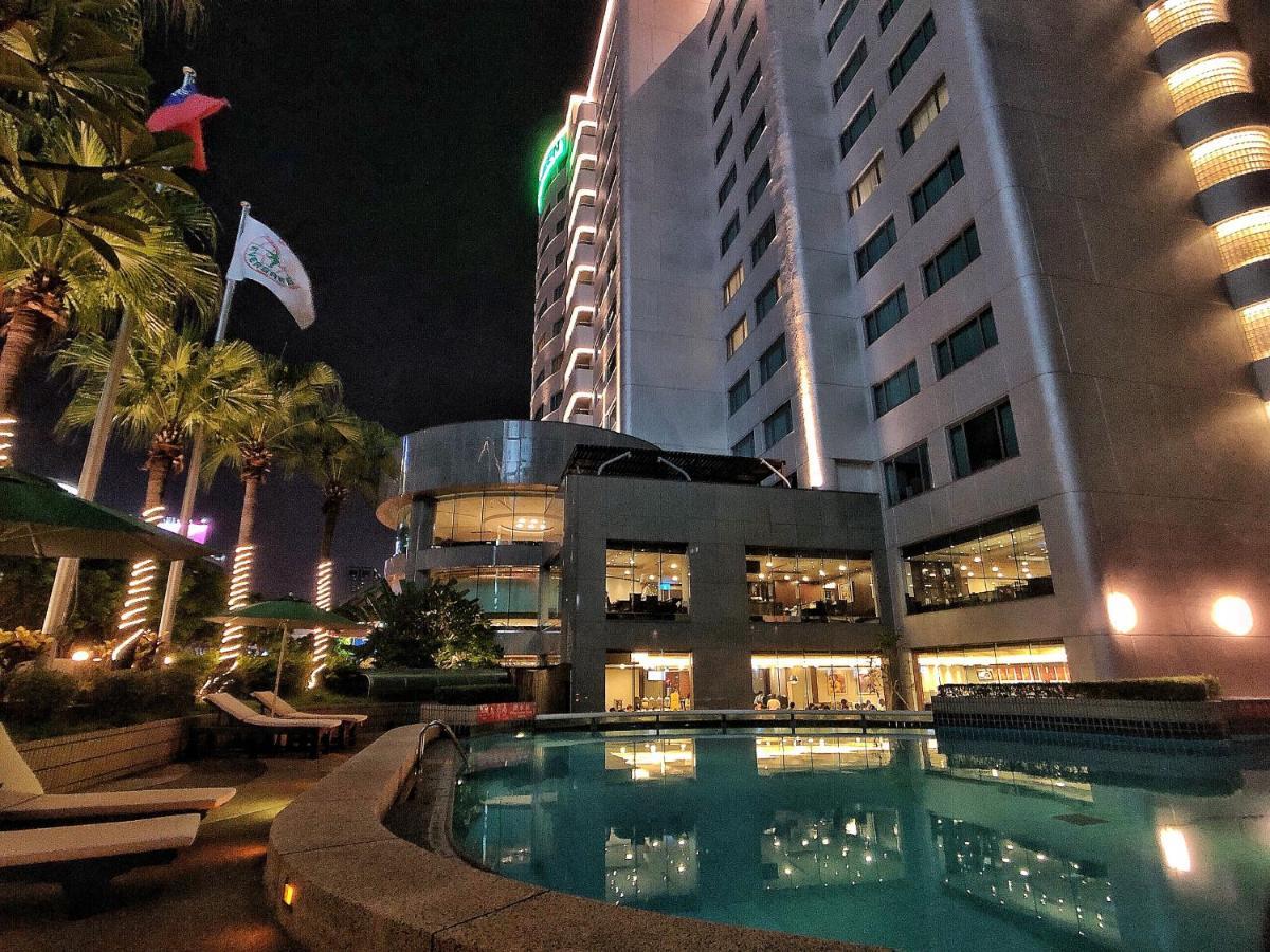 เอเวอร์กรีน เลาเรล โฮเต็ล ไทชุง Hotel ไถจง ภายนอก รูปภาพ The photo depicts a modern hotel or building at night, featuring a sleek facade illuminated by lights. In the foreground, there is a swimming pool that reflects the surrounding lights and palm trees. There are lounge chairs near the pool, and the atm